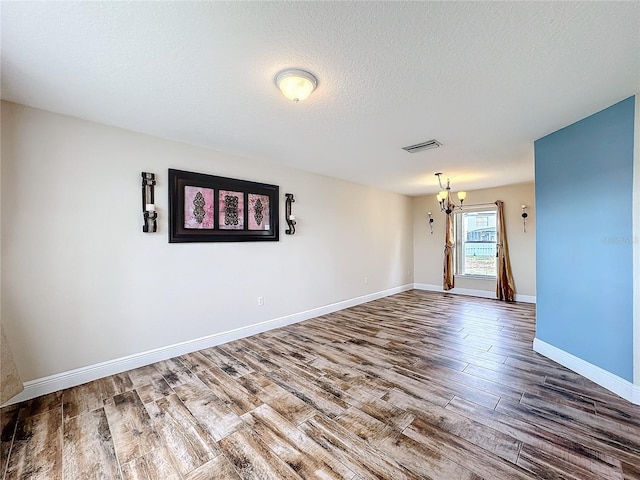 spare room featuring wood-type flooring, a textured ceiling, and a notable chandelier