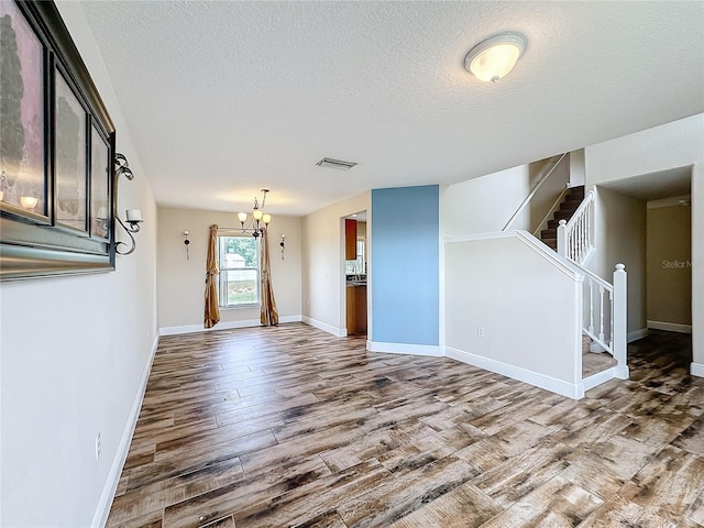 unfurnished living room featuring a chandelier, a textured ceiling, and hardwood / wood-style flooring