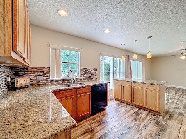 kitchen with backsplash, light stone counters, sink, decorative light fixtures, and black dishwasher