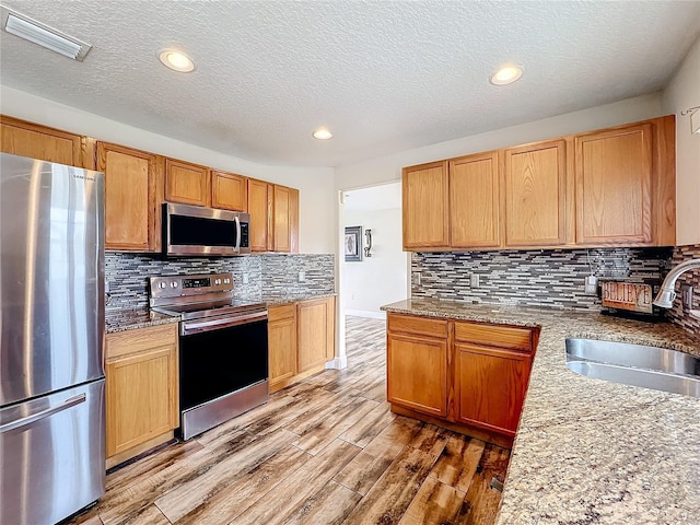 kitchen with light stone countertops, sink, a textured ceiling, decorative backsplash, and appliances with stainless steel finishes