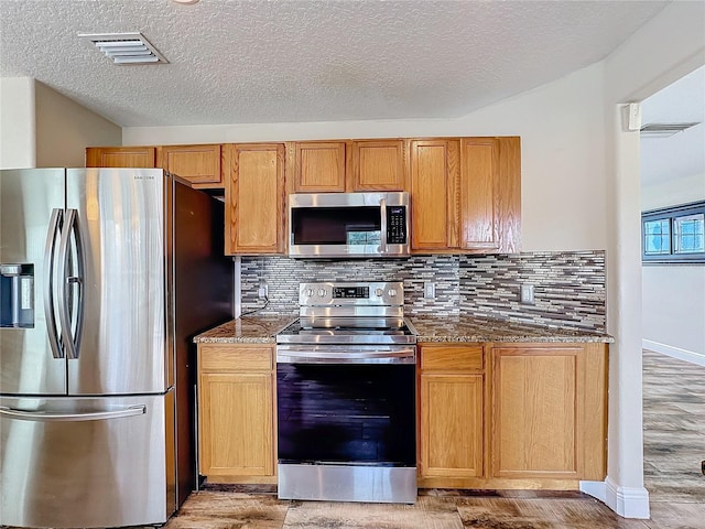 kitchen with tasteful backsplash, light wood-type flooring, a textured ceiling, and appliances with stainless steel finishes