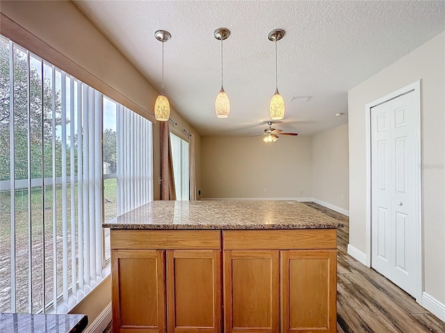 kitchen with ceiling fan, light stone counters, hardwood / wood-style floors, a textured ceiling, and decorative light fixtures