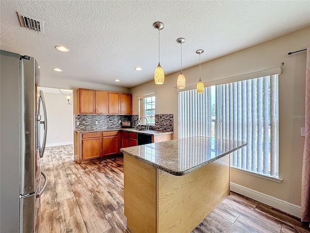 kitchen with tasteful backsplash, stainless steel fridge, dark stone counters, pendant lighting, and light wood-type flooring