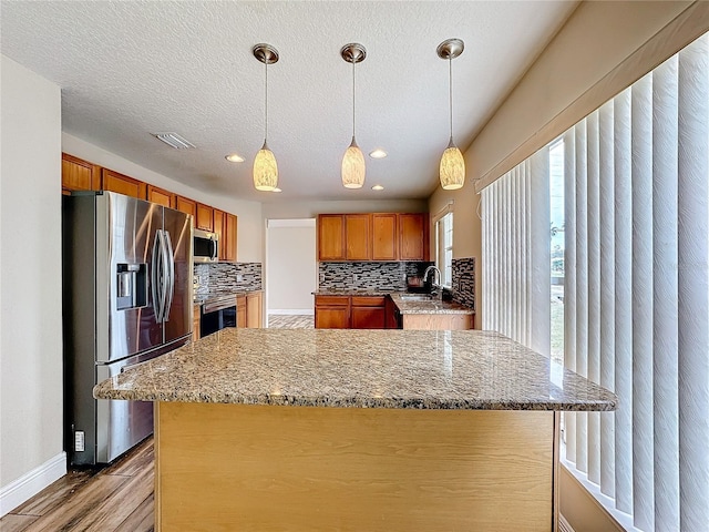 kitchen with backsplash, light stone counters, stainless steel appliances, sink, and decorative light fixtures