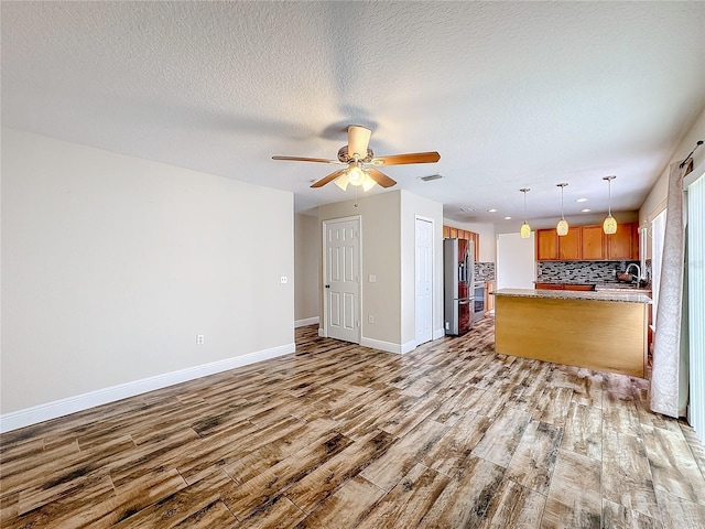 kitchen featuring backsplash, stainless steel fridge with ice dispenser, hanging light fixtures, and light wood-type flooring