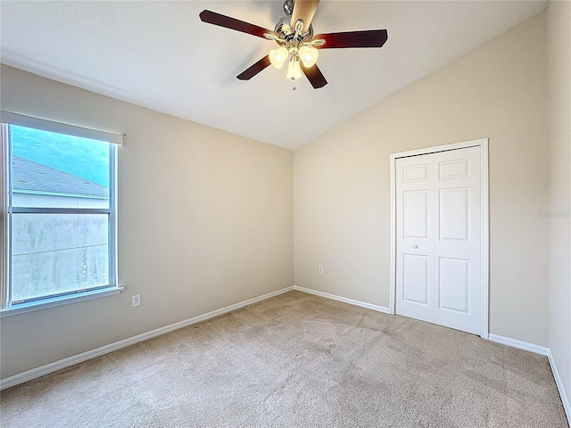 unfurnished bedroom featuring ceiling fan, lofted ceiling, multiple windows, light carpet, and a closet