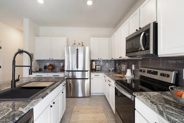 kitchen with light tile patterned flooring, stainless steel appliances, white cabinetry, and dark stone countertops