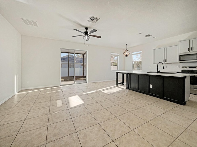 kitchen with a kitchen island with sink, white cabinets, ceiling fan with notable chandelier, sink, and appliances with stainless steel finishes