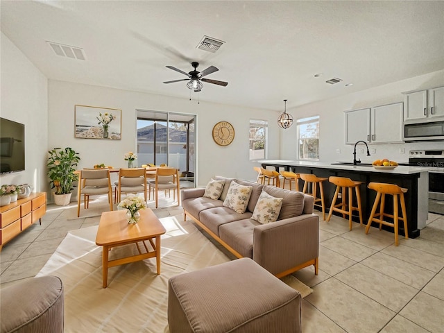 living room featuring a wealth of natural light, sink, light tile patterned floors, and ceiling fan with notable chandelier