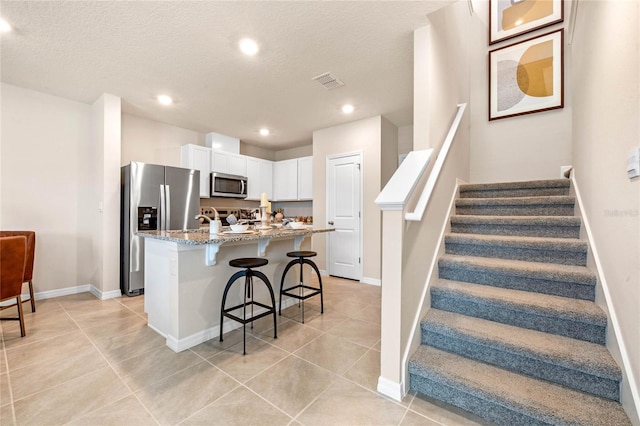 kitchen with white cabinetry, light stone countertops, an island with sink, a breakfast bar area, and appliances with stainless steel finishes