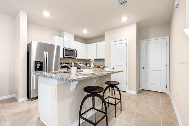 kitchen with a kitchen island with sink, a breakfast bar area, light stone counters, white cabinetry, and stainless steel appliances