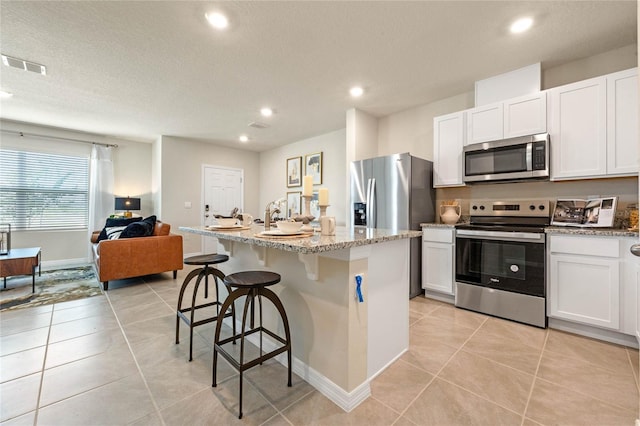 kitchen with appliances with stainless steel finishes, white cabinetry, light stone counters, and a kitchen island with sink