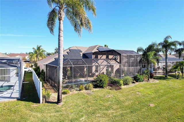 back of house featuring solar panels, glass enclosure, and a lawn