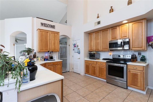 kitchen featuring tasteful backsplash, light tile patterned floors, stainless steel appliances, and high vaulted ceiling