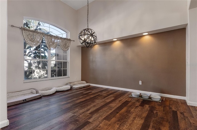 unfurnished dining area featuring dark wood-type flooring, a high ceiling, and an inviting chandelier