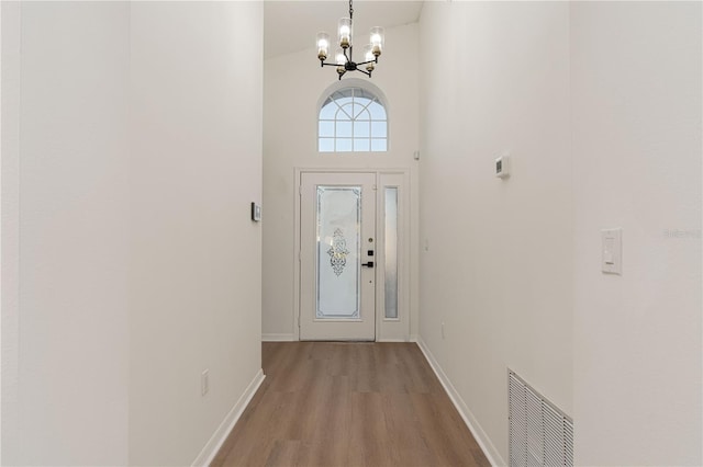 doorway featuring a towering ceiling, light hardwood / wood-style floors, and a notable chandelier