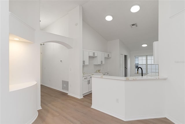 kitchen featuring kitchen peninsula, tasteful backsplash, high vaulted ceiling, light hardwood / wood-style flooring, and white cabinets