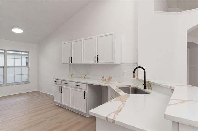 kitchen featuring backsplash, white cabinets, sink, vaulted ceiling, and kitchen peninsula