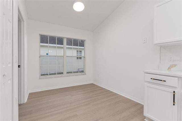 unfurnished dining area with light wood-type flooring and vaulted ceiling