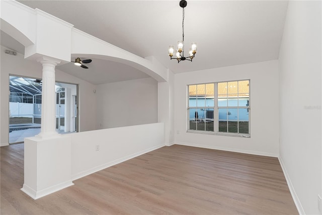 empty room featuring decorative columns, lofted ceiling, light hardwood / wood-style flooring, and ceiling fan with notable chandelier