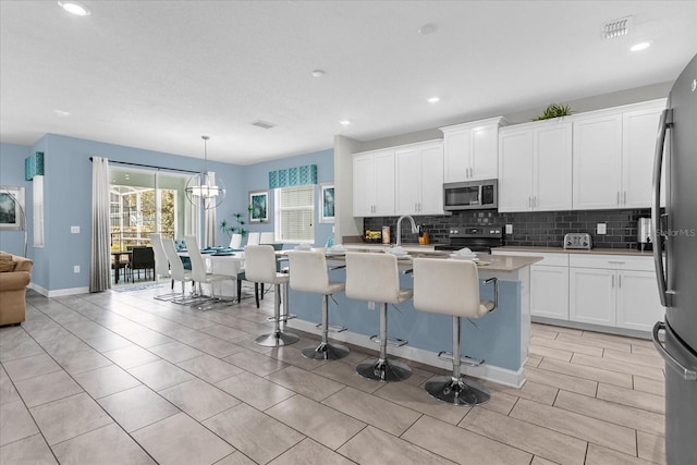 kitchen with appliances with stainless steel finishes, a kitchen island with sink, white cabinets, hanging light fixtures, and a breakfast bar area