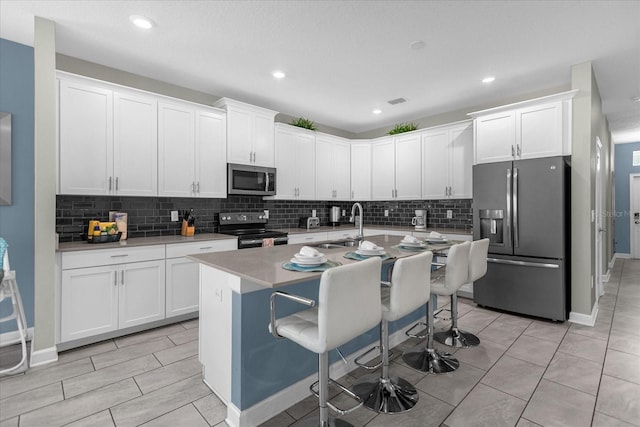 kitchen with sink, a kitchen island with sink, a breakfast bar, white cabinets, and appliances with stainless steel finishes