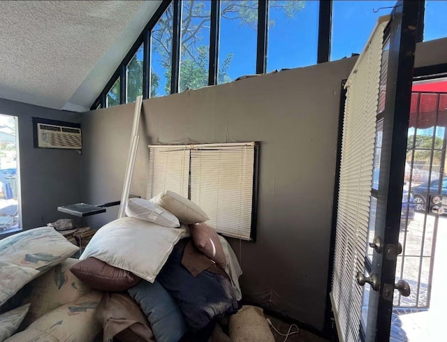 interior space with a textured ceiling, high vaulted ceiling, a wall unit AC, and multiple windows