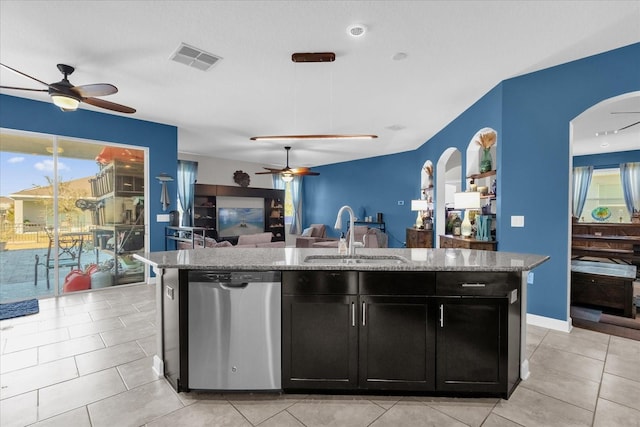 kitchen with light stone countertops, stainless steel dishwasher, sink, a center island with sink, and light tile patterned flooring