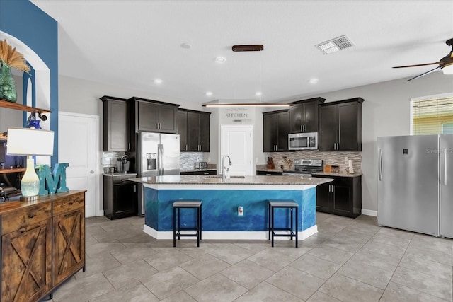 kitchen featuring a kitchen breakfast bar, light stone countertops, a center island with sink, and stainless steel appliances