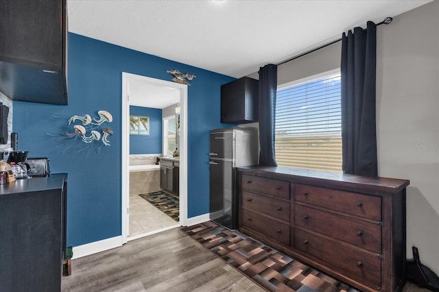 bedroom featuring ensuite bath, stainless steel fridge, and dark hardwood / wood-style floors