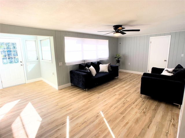 living room with ceiling fan, wooden walls, and light hardwood / wood-style floors