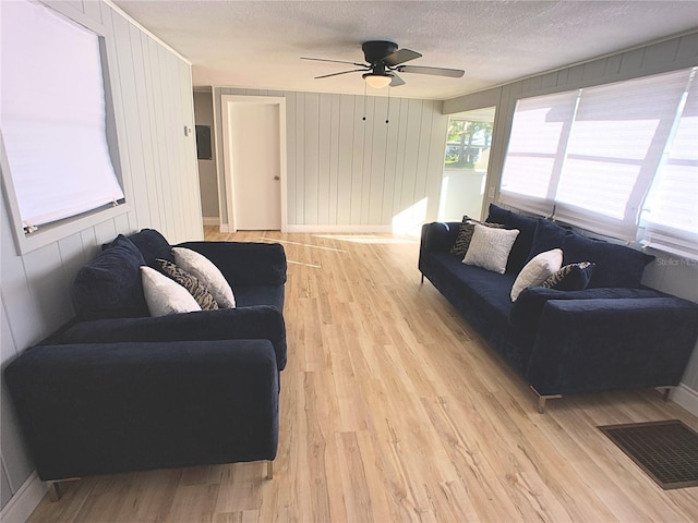 living room with ceiling fan, wood walls, light wood-type flooring, and a textured ceiling