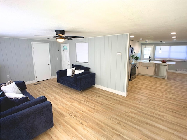 living room with light hardwood / wood-style floors, ceiling fan, wood walls, and sink