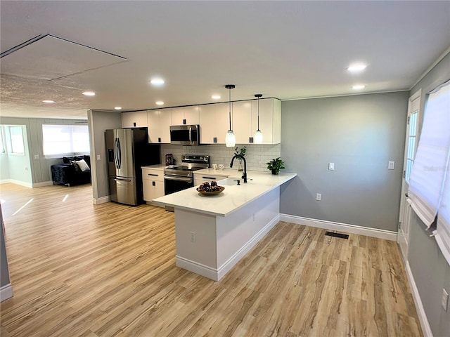 kitchen featuring tasteful backsplash, kitchen peninsula, pendant lighting, white cabinets, and appliances with stainless steel finishes