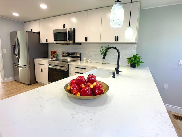 kitchen with appliances with stainless steel finishes, backsplash, white cabinetry, and pendant lighting