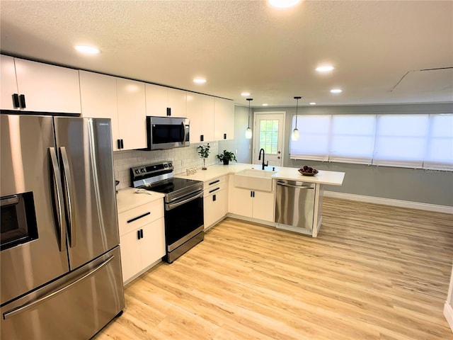 kitchen featuring kitchen peninsula, sink, appliances with stainless steel finishes, decorative light fixtures, and white cabinetry