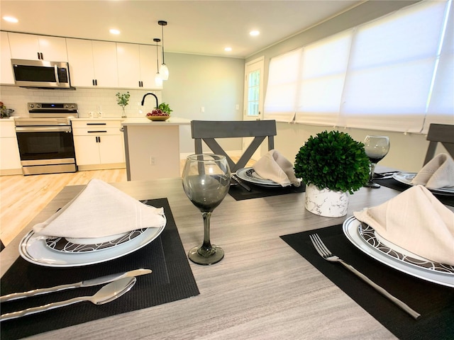 interior space featuring white cabinets, decorative light fixtures, light hardwood / wood-style floors, and stainless steel appliances