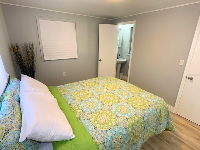 bedroom with ensuite bath, ornamental molding, and light wood-type flooring