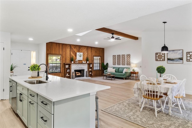 kitchen featuring sink, wooden walls, decorative light fixtures, stainless steel dishwasher, and a center island with sink