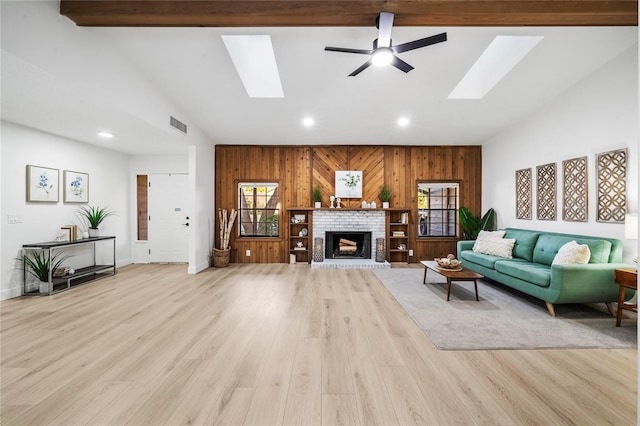 living room with light hardwood / wood-style flooring, wood walls, vaulted ceiling with skylight, a fireplace, and ceiling fan