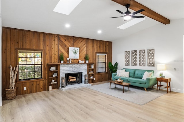 living room featuring lofted ceiling with skylight, wooden walls, ceiling fan, and light wood-type flooring