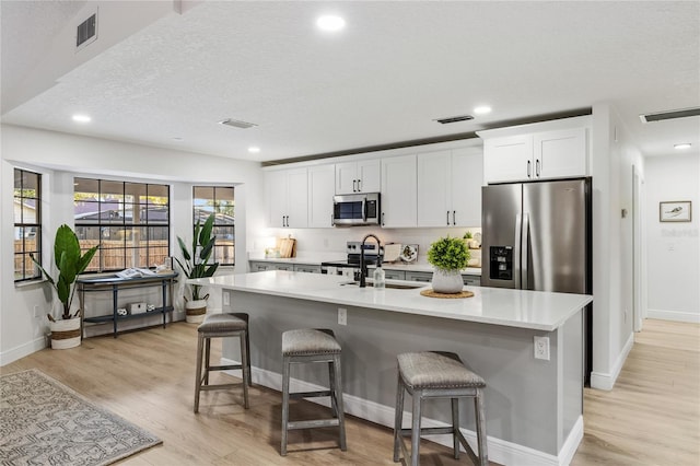 kitchen featuring a center island with sink, white cabinets, a breakfast bar, and appliances with stainless steel finishes