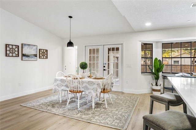 dining space featuring french doors, a textured ceiling, vaulted ceiling, and light hardwood / wood-style floors