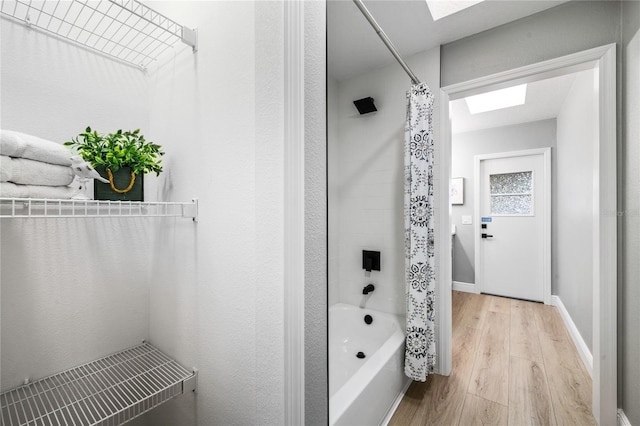 bathroom featuring hardwood / wood-style flooring, shower / bathtub combination with curtain, and a skylight