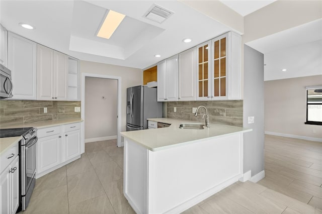 kitchen with kitchen peninsula, appliances with stainless steel finishes, a raised ceiling, sink, and white cabinets