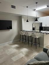 bar with stainless steel fridge with ice dispenser, decorative backsplash, white cabinetry, and hanging light fixtures