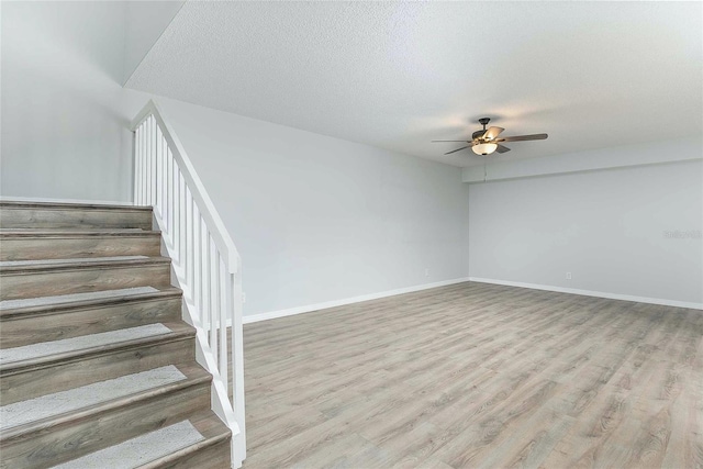 stairway with ceiling fan, a textured ceiling, and hardwood / wood-style flooring