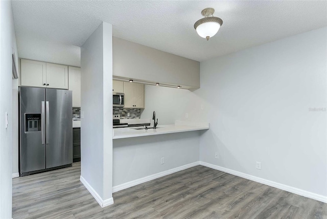 kitchen featuring sink, tasteful backsplash, light hardwood / wood-style flooring, a textured ceiling, and appliances with stainless steel finishes