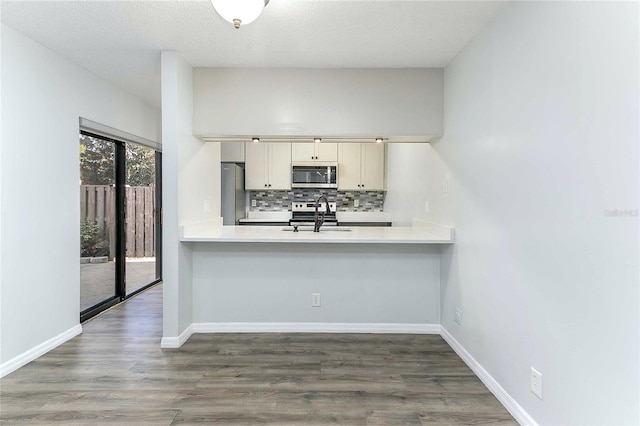 kitchen featuring dark wood-type flooring, sink, decorative backsplash, kitchen peninsula, and stainless steel appliances