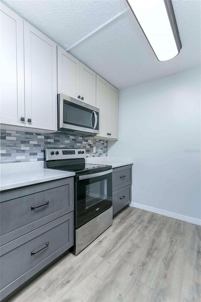 kitchen with white cabinets, gray cabinetry, backsplash, and appliances with stainless steel finishes